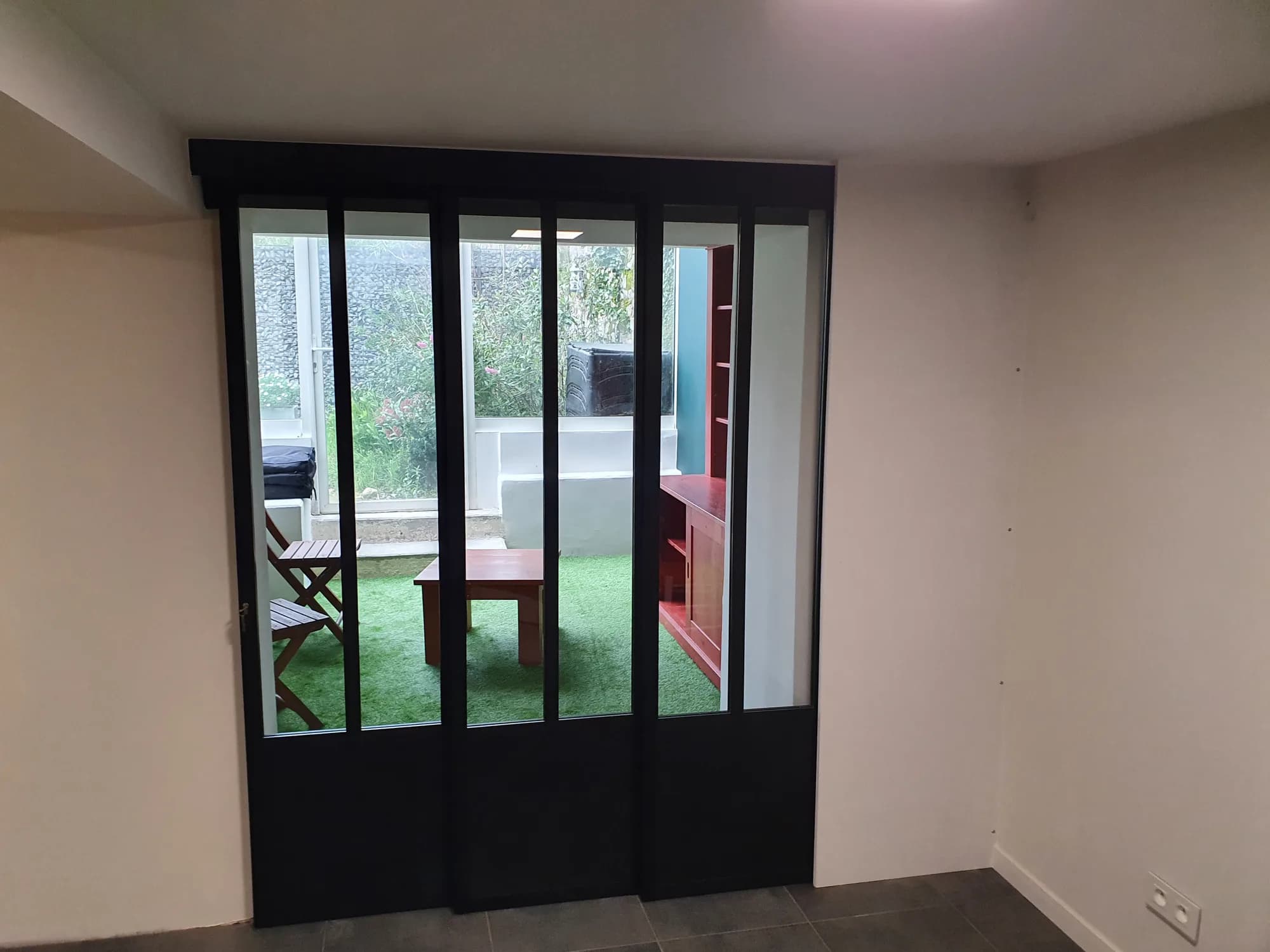 Verrière d'atelier en acier noir sur mesure ouvrant sur une véranda et un jardin